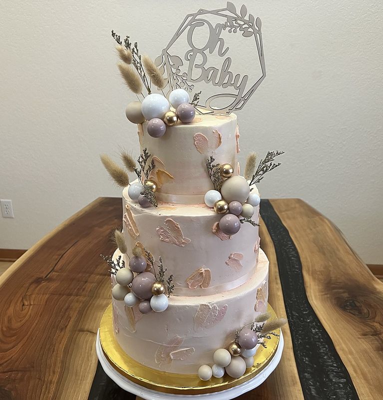 Three-tier blush baby shower cake with an Oh Baby topper, dried bunny-tail grass and pearl spheres