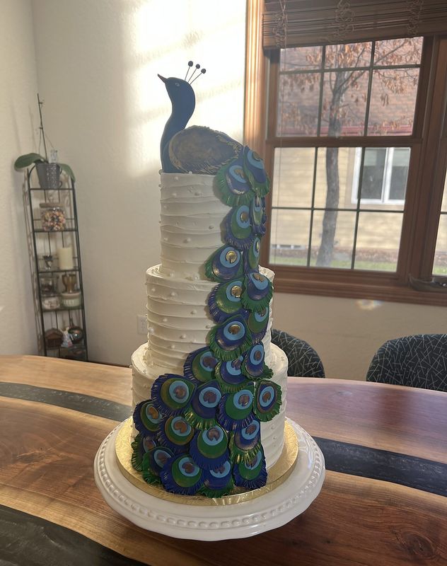 Tall four-tier white textured cake with a hand-sculpted peacock trailing down the tiers
